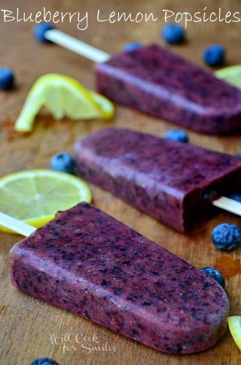 Blueberry lemon popsicles on a cutting board with lemons and blueberries 