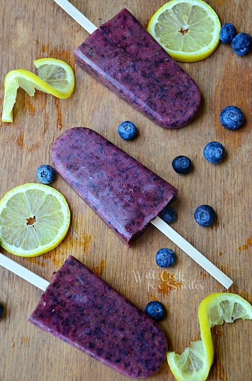 above photo of Blueberry lemon popsicles on a wood cutting board with slices lemons and blueberries 
