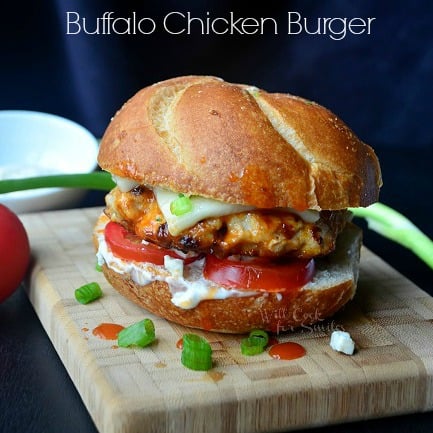 Buffalo Chicken Burger on a bun with cheese, tomato, and blue cheese dressing on a cutting board 