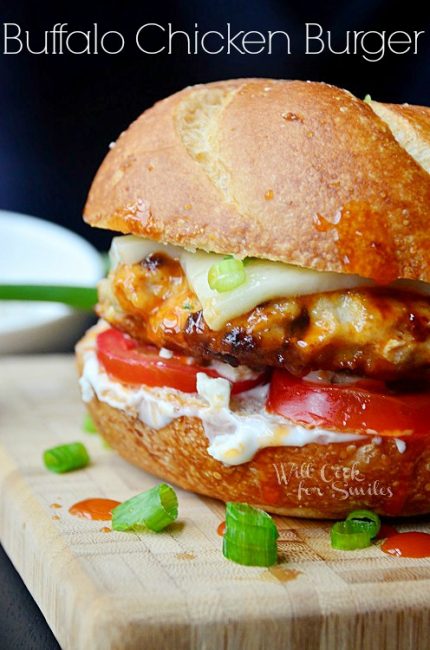 Buffalo Chicken Burger on a bun with cheese, tomato, and blue cheese dressing on a cutting board 