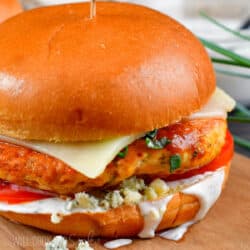 closeup of a buffalo chicken burger on a bun with sliced of cheese, blue cheese crumbles.