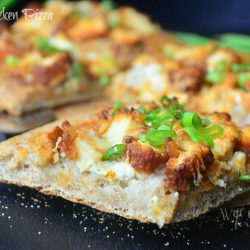 Sliced buffalo chicken pizza on cutting board with pizza cutter below slice to the left