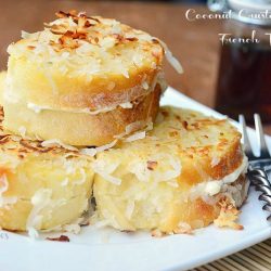 stacked coconut stuffed french toast on white square plate with fork at bottom right and bottle of syrup in background to right