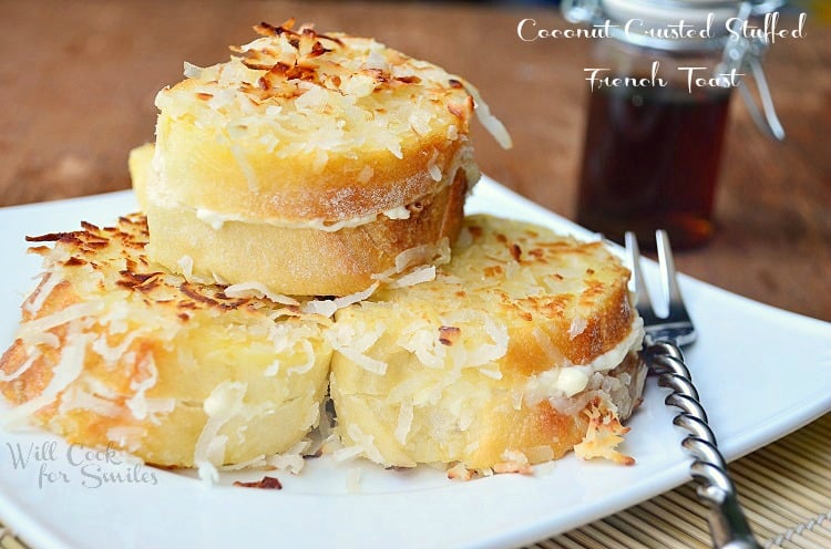 stacked coconut stuffed french toast on white square plate with fork at bottom right and bottle of syrup in background to right