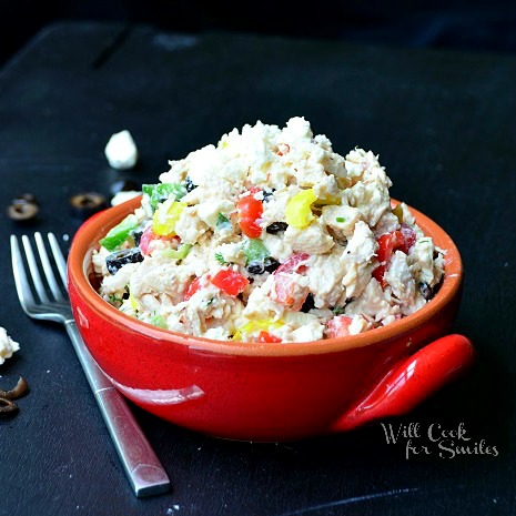 greek chicken salad in a red bowl in the center and a fork next to it