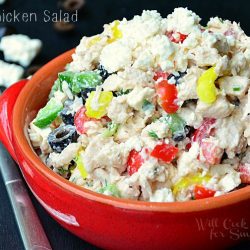 red clay bowl filled with greek chicken salad on black table with fork above left