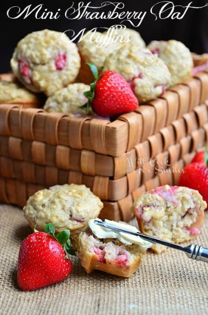 strawberry Oat Muffins on a table clothe with one cut in half and a knife buttering on of them and strawberry next to it and the rest in a basket 