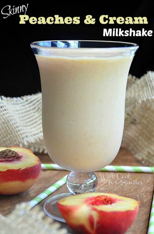 peaches and cream milkshake in a glass with a peach cut in half on the wood table