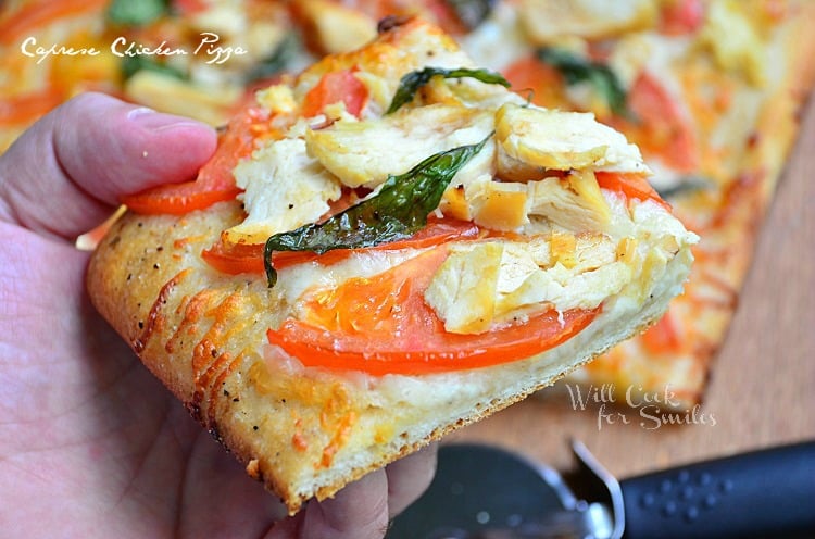 holding a Caprese Chicken Pizza with chicken, tomato, and basil slice 