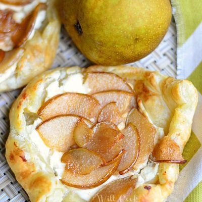 3 caramel pear pastries on table cloth with white and yellow cloth to right and 2 pears in background