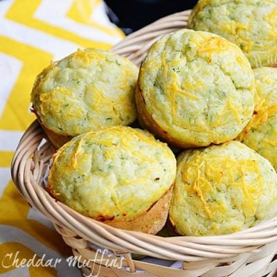 light brown wicker basket filled with zucchini cheddar muffins and 2 muffins below basket