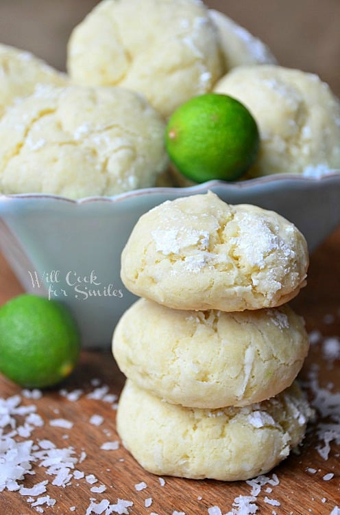 stack of three cookies next to a blue bowl of cookies and a couple key limes