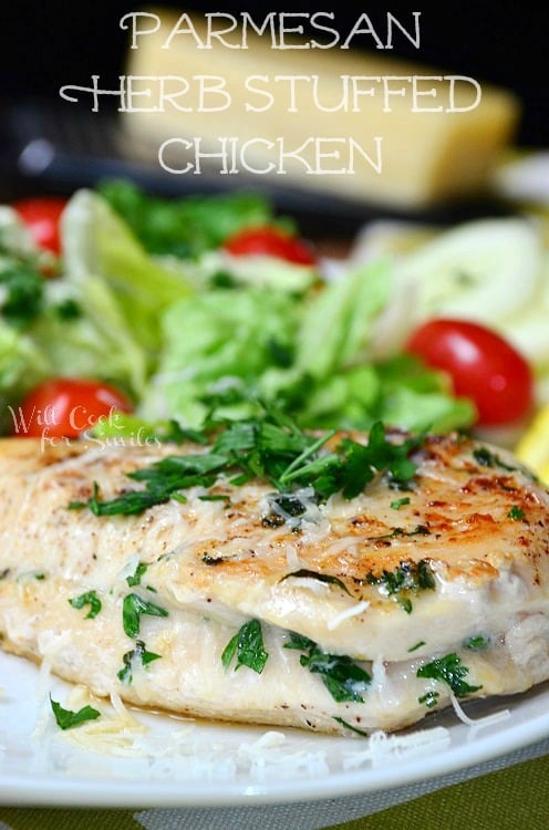 Parmesan and Herb Stuffed Chicken on a plate with herbs on the top and a lettuce with tomato salad on the side 