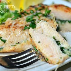 1 portion of parmesan herb stuffed chicken on white plate with empty wine glass in background and block of cheese and grater in background to the left