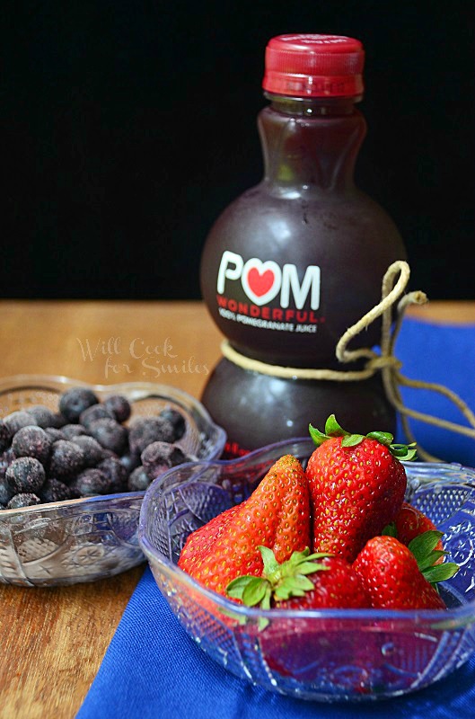 blueberries and strawberries in a bowl and Pomegranate juice in a small container 