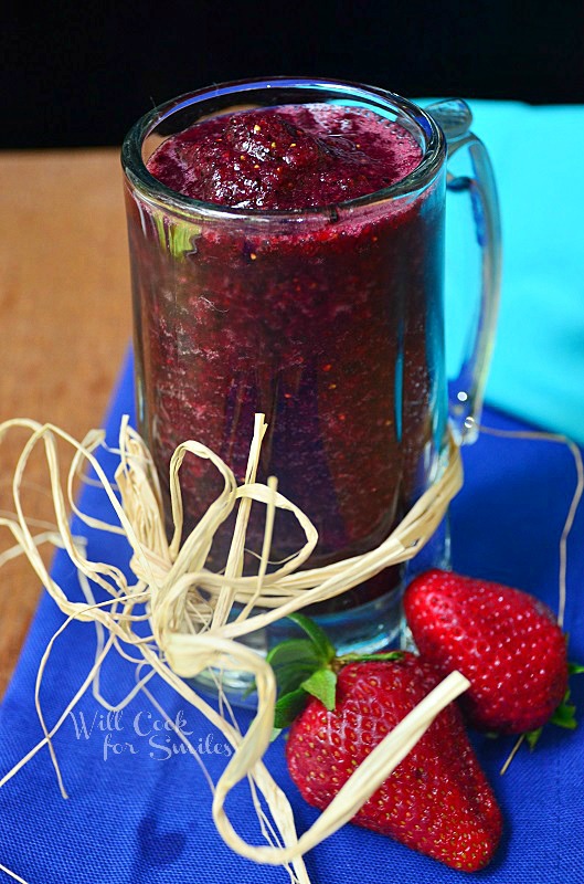 Pomegranate smoothie in a glass much with twine wrapped around the bottom of the outside of the mug with strawberries to the left 