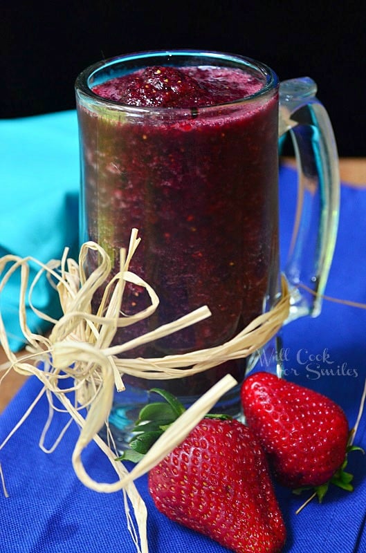 Pomegranate smoothie in a glass much with twine wrapped around the bottom of the outside of the mug with strawberries to the left 