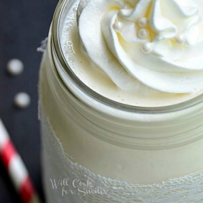 close up picture of mason jar filled with white wedding cake milkshake on a black table with red and white striped straws laying around jar