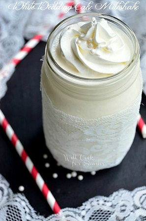 white wedding cake milkshake in a mason jar with whipped cream and candy pearls on top 