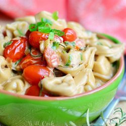 green and red clay bowl filled with creamy rosemary tomato tortellini on a burlap mat with fork to the bottom right