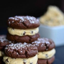 several chocolate cookies filled with chocolate chip cookie dough and white square bowl with cookie dough to left of cookies
