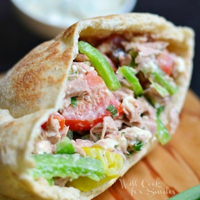 open face of greek tuna pita on wood cutting board with white bowl and sauce in background