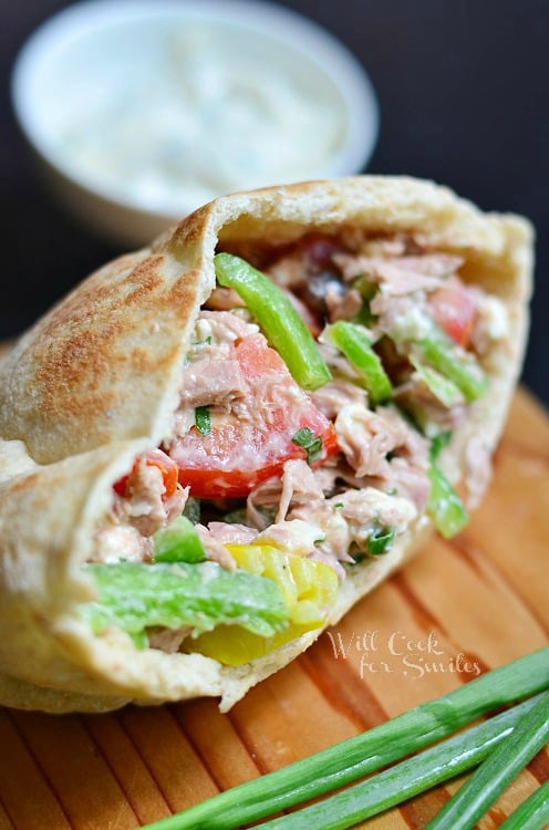 open face of greek tuna pita on wood cutting board with white bowl and sauce in background
