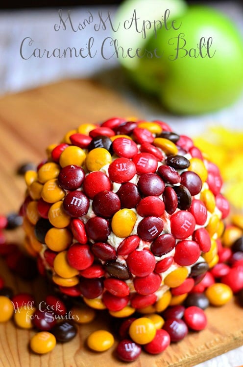 M&M Caramel Apple Dessert Cheese Ball on a wood cutting board with green apples in the background 