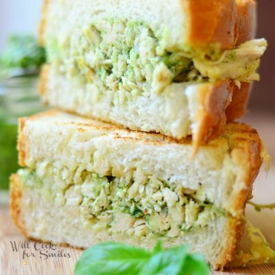 half of sandwich on top of the ther half dilled with pesto chicken salad and leaves of basil next to it