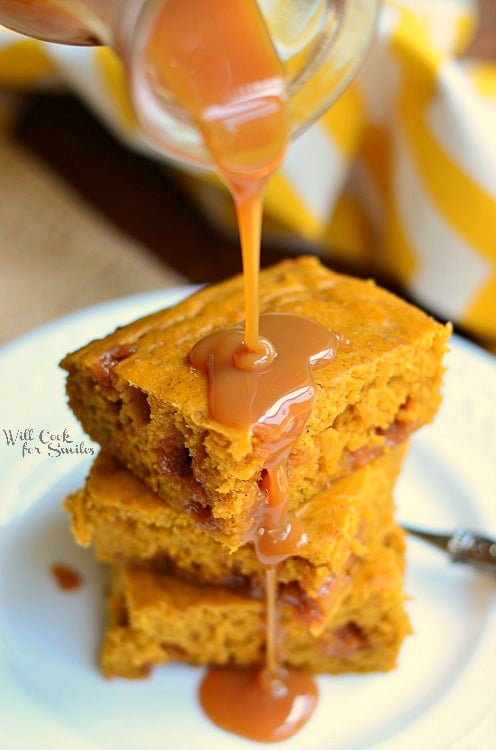 Pumpkin Caramel Blondies stacked on a plate with caramel being poured over them 