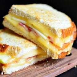 2 halves of apple bacon gouda grilled cheese stacked on each other on wood cutting board