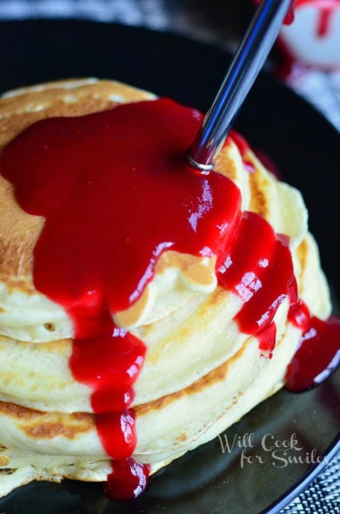above photo of stack of pancakes with strawberry syrup and a fork in them 