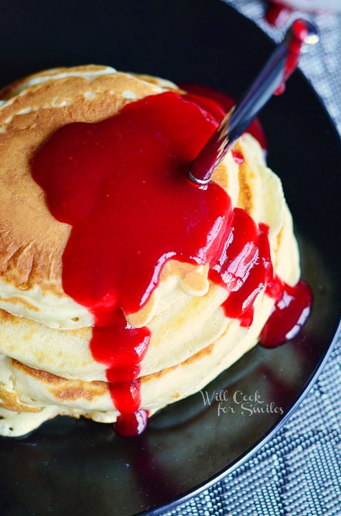 above photo of stack of pancakes with strawberry syrup and a fork in them 