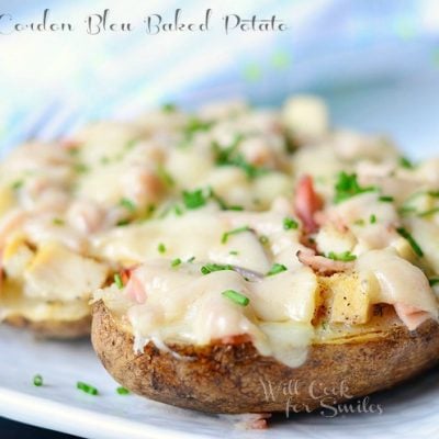 close up picture of 2 chicken cordon bleu baked potatoes on white plate topped with chopped parsley