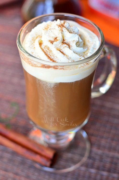 Cinnamon Dolce Coffee Drink in a glass cup with cinnamon sticks on the table next to it 