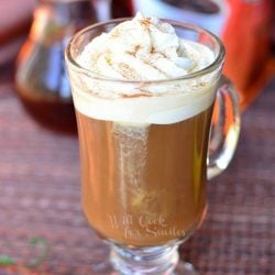 dessert coffee glass mug filled with cinnamon dolce coffee drink on placemat with 2 cinamon sticks at bottom left coffee bag inbackground