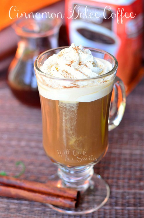 dessert coffee glass mug filled with cinnamon dolce coffee drink on placemat with 2 cinamon sticks at bottom left coffee bag inbackground