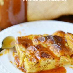1 portion of pimpkin bread pudding on white plate with sauce in mason jar to the left and tan cloth in background to the right