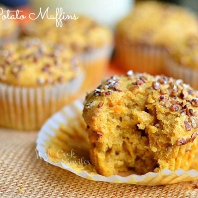 close up view of sweet potato muffins on burlap table cloth with jug of milk in background all on orange colored wood table