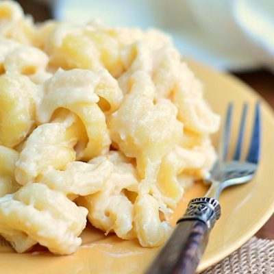 1 portion of zesty mac and cheese on yellow plate with white cloth in background and fork on plate