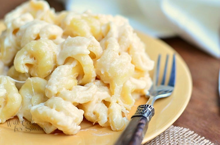 1 portion of zesty mac and cheese on yellow plate with white cloth in background and fork on plate