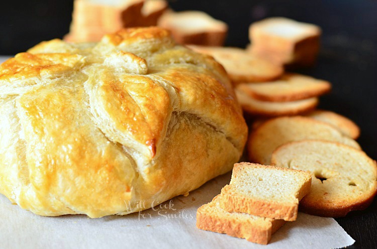 baked brie on a piece of wax paper on a cutting board with bread 