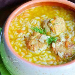 clay soup crock with chicken orzo soup on a light green napkin with a spoon at the right of crock all on wood table