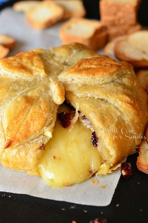 Cranberry Maple Baked Brie on a wax paper with a slice cut out of it 