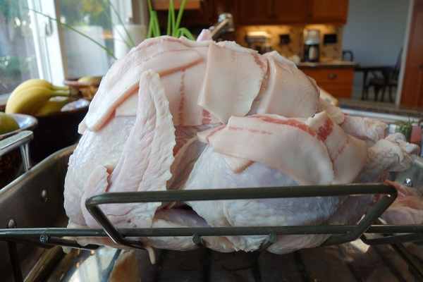 uncooked turkey in a roasting pan with bacon on top 
