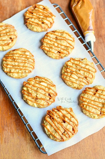 apple oatmeal cookies with caramel drizzled over the top on wax paper on top of a cooling rack 