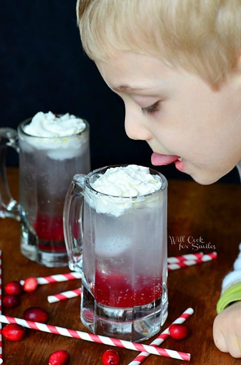 boy licking whipped cream off of Cranberry Italian Soda in a glass mug 