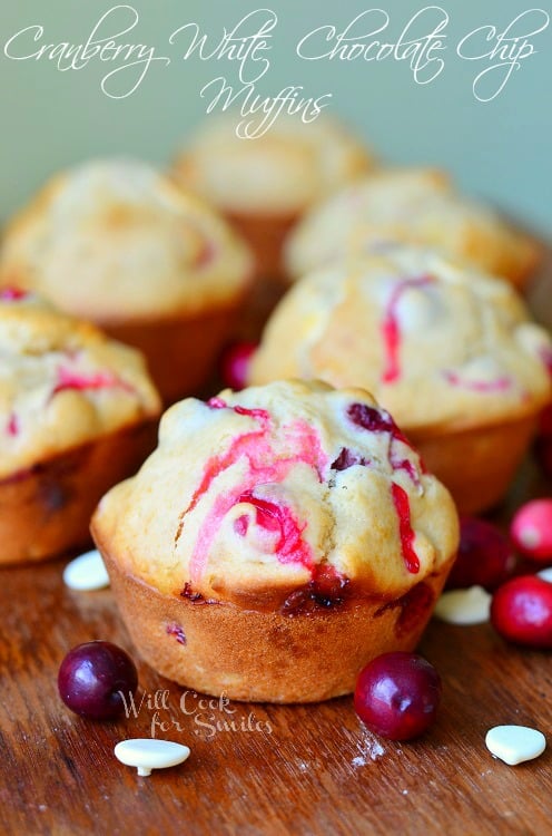 Cranberry White Chocolate Chip Muffins on a table with cranberries and white chocolate chips around it 