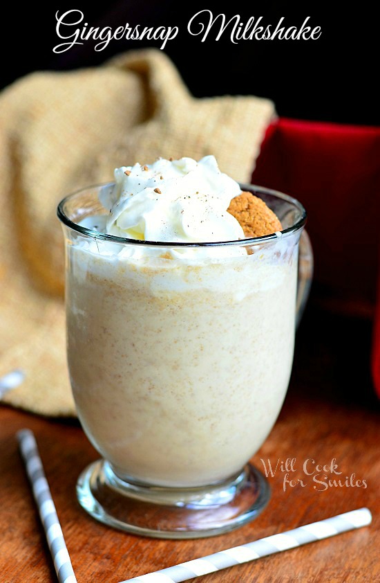 Gingersnap Milkshake in a glass with whipped cream and a ginger bread cookie as garnish on a wood table with white and blue paper straws 