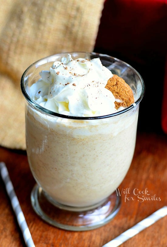 Gingersnap Milkshake in a glass with whipped cream and a ginger bread cookie as garnish on a wood table with white and blue paper straws 
